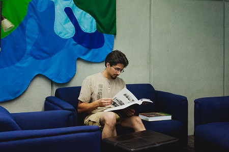 Male student reading on couch in library